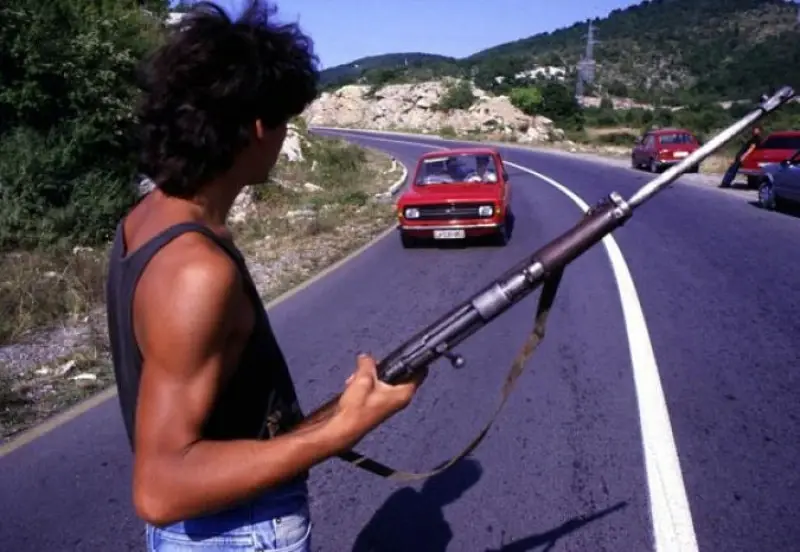 Тридесет година геноцида - Срби на барикадама. Човек држи пушку док му прилази сутомобил.
